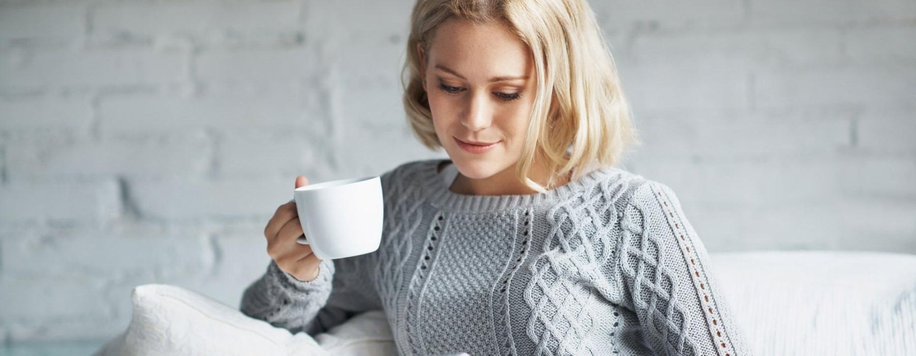 a woman sits on a couch with a cup of coffee and looks at her tablet